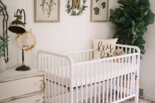 a neutral vintage nursery with white shabby furniture, a statement plant, artworks and a vintage lamp