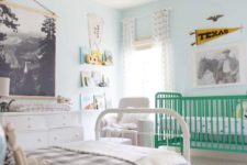 a pastel shared nursery with light blue walls, a green crib, a white bed and other furniture and cool artworks