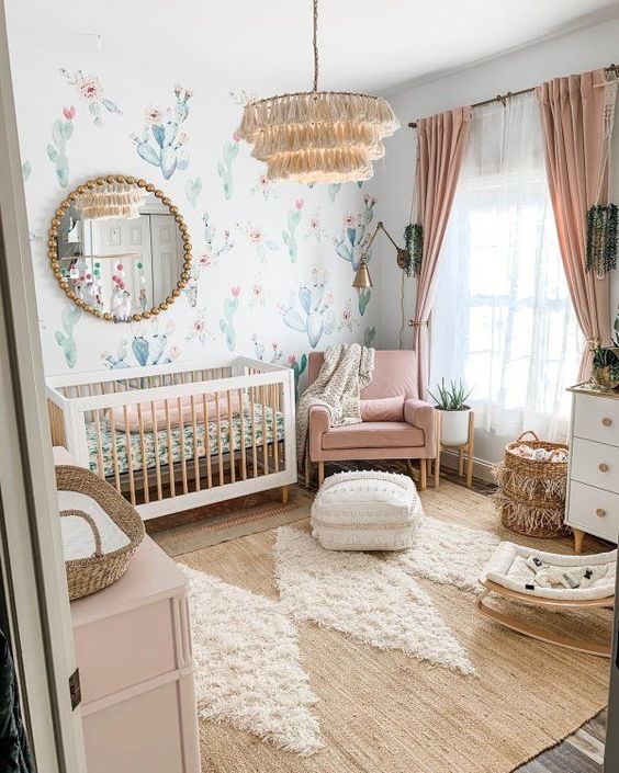 a pretty boho girlish nursery with a cactus wall, neutral and pink furniture, pink bedding and curtains, a tassel chandelier and a lovely boho rug