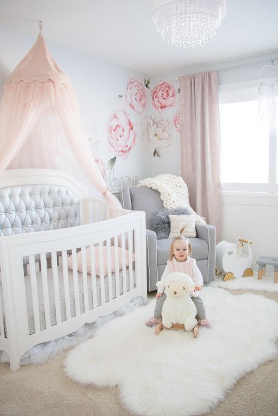 a pretty nursery with light blue walls, floral decals, white and grey furniture, a pink canopy and pink curtains plus a crystal chandelier