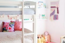 a pretty shared girls’ bedroom with a white bunk bed, an ombre accent wall, bookshelves and a macrame hanging, toys and a bold rug