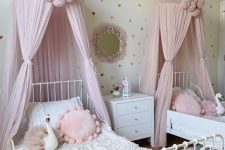 a princess-style shared girls’ bedroom with a white metal bed, pink canopies, pink pillows, a white nightstand and a mirror in a pink frame