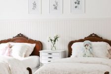 a refined French cottage shared girls’ bedroom with paneling, dark stained carved wooden beds, a white nightstand and a gallery wall with botanicals