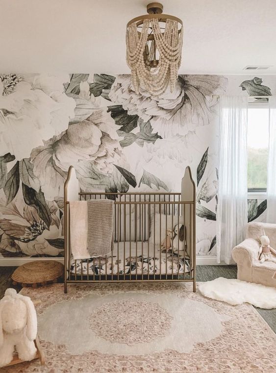 a refined girl nursery with a floral mural, a vintage brass crib, neutral and pink textiles and a beaded chandelier