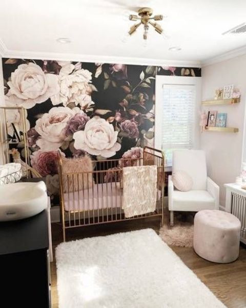 a refined moody girl nursery with a moody floral wall, white and black furniture, a brass crib, blush and white textiles