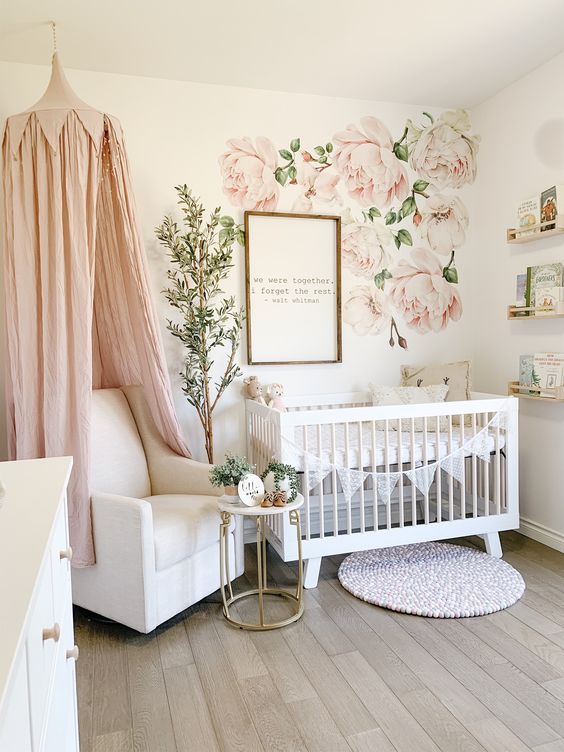 a romantic girlish nrusery with floral decals, white furniture, a pink canopy over the chair and some open shelves