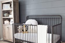a rustic gender neutral nursery with a grey accent wall, a reclaimed wood storage unit and a black metal crib