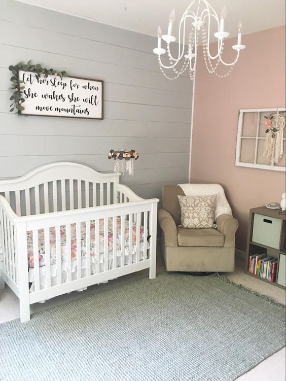 a rustic girlish nursery with a pink and grey wall, a lovely sign, white and taupe furniture, a vintage chandelier and some shabby chic decor