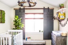 a rustic nursery with sliding shutters, a wooden chandelier, a weathered dresser and prints is a welcoming space