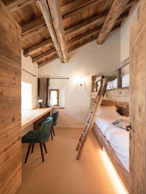 a rustic shared boy bedroom with rough wood bunk beds, a floating desk, woodne beams and a ladder