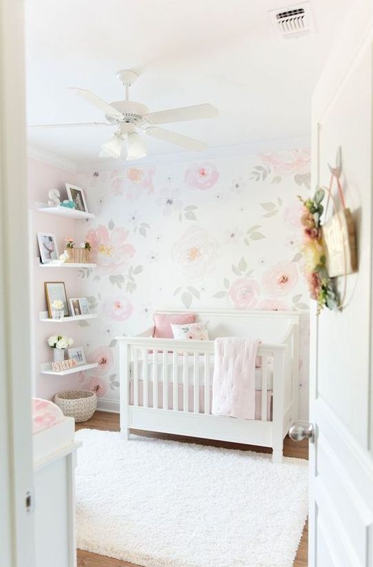 a simple and chic girlish nursery with white furniture, a floral wall, open shelves and white and pink bedding