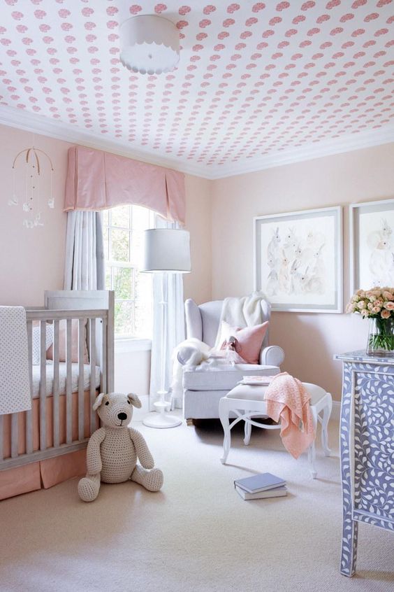 a simple pastel nursery with blush walls, grey and blue furniture, a printed ceiling, pastel pink textiles and bedding and a gallery wall