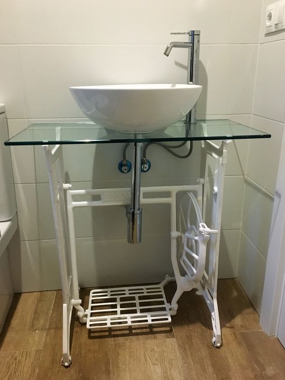 a sink stand made of a Zinger sewing machine, with a glass countertop is a unique and bold way to add a vintage touch to your modern bathroom