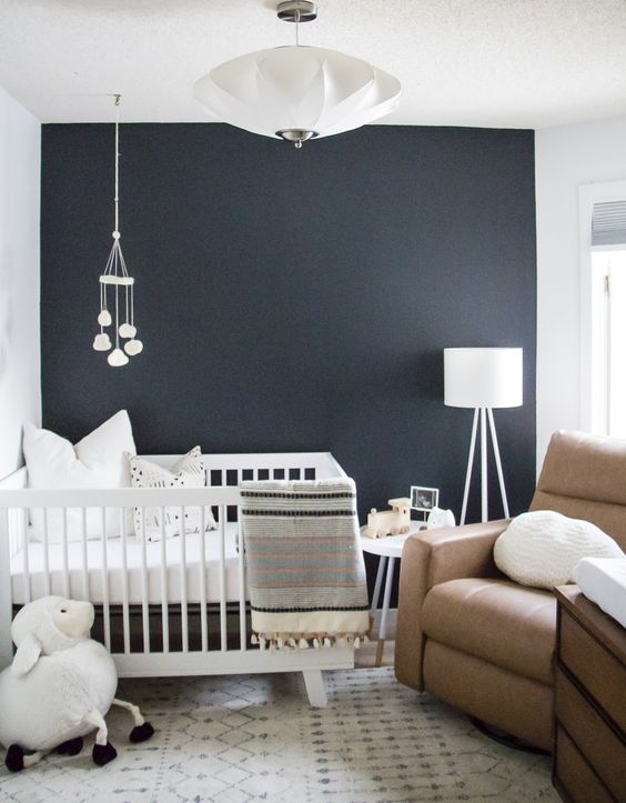 a small yet welcoming nursery with a navy accent wall, a brown leather chair and some white furniture