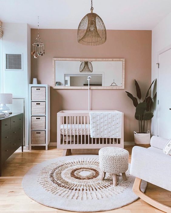 a stylish boho nursery with a pink accent wall, neutral furniture, a green dresser, a wicker pendant lamp and neutral textiles