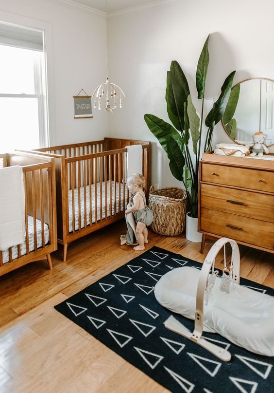 A stylish mid century modern nursery with rich stained furniture, a basket, a statement plant and a cool printed rug
