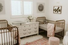 a stylish shared nursery with a vintage feel, with metal cribs, neutral furniture, a floral chandelier and printed rug