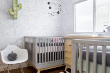 a stylish shared nursery with pinted wallpaper, grey and stained furniture, a printed rug and grey bedding