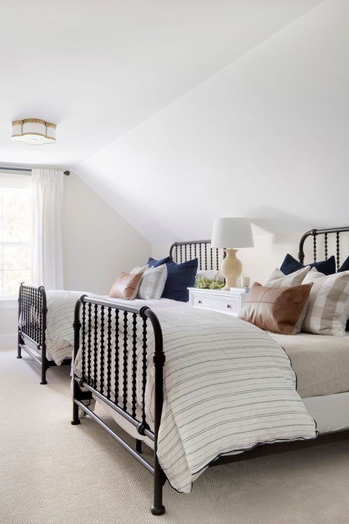 a stylish traditional attic shared bedroom with metal beds, a sideboard as a nightstand, printed bedding