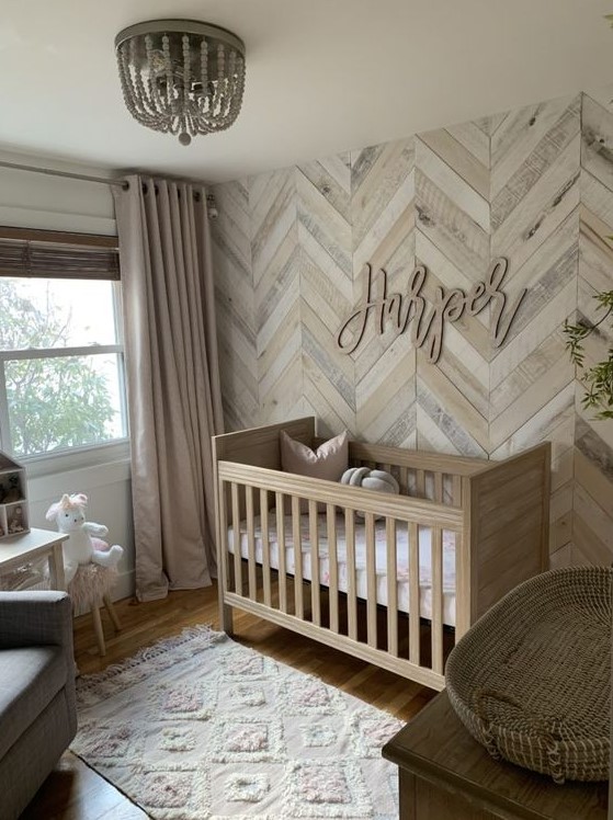a warm neutral farmhouse nursery with a reclaimed wooden wall with a herringbone pattern, a bead chandelier, a cool rug and a stained crib