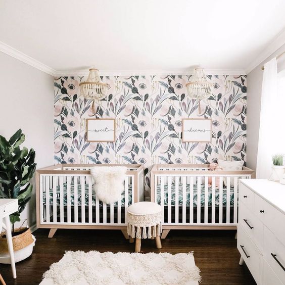 a welcoming neutral nursery with a botanical accent wall, neutral furniture, a potted plant and beaded chandeliers for decor