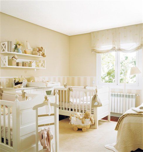 a welcoming neutral shared nursery with tan walls, white furniture and lots of toys everywhere