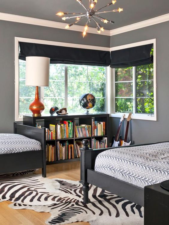 a whimsical shared boy bedroom with black curtains, black furniture, a faux animal skin rug and some lamps
