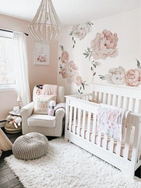an airy neutral nursery with a floral mural, white furniture, a beaded chandelier, neutral textiles and pretty toys