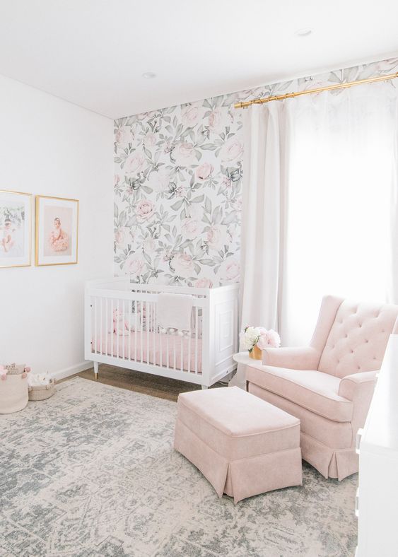 an airy nursery with a floral wall, a pink chair and ottoman, pink bedding and a boho rug is cool