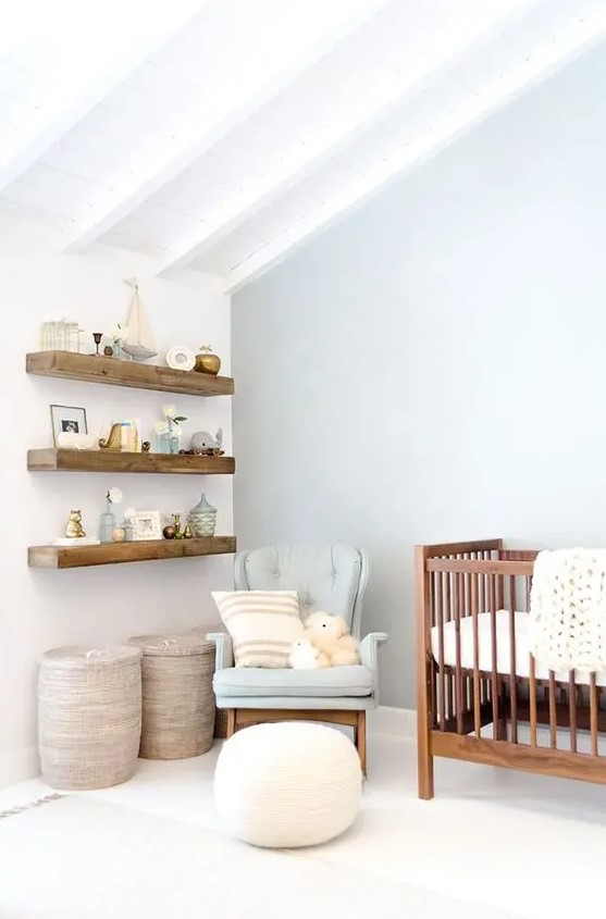 an airy pastel attic nursery with wooden beams, a stained crib and wall-mounted shelves, a grey chair and neutral textiles