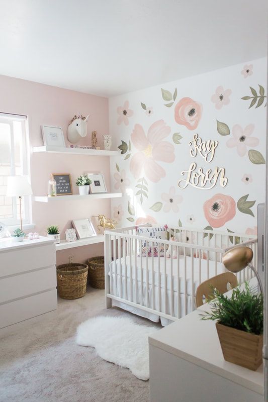 an amazing modern girl nursery with a floral accent wall, white furniture, gold and brass touches and potted greenery