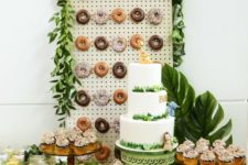 a jungle-themed dessert table with a donut wall, tropical leaves, lots of greenery and a large cake is a chic idea