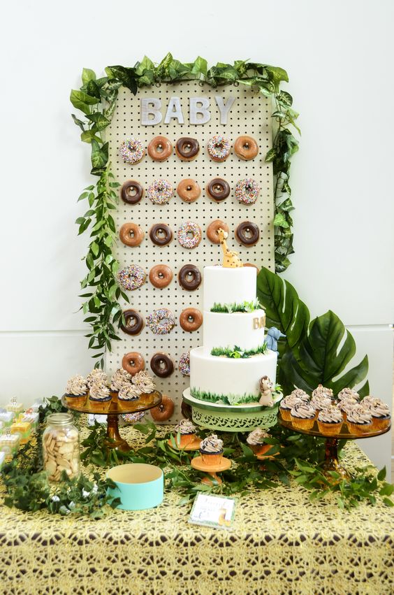 A jungle themed dessert table with a donut wall, tropical leaves, lots of greenery and a large cake is a chic idea