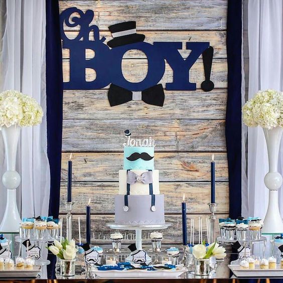 a rustic boy's baby shower dessert table with navy candles, white floral arrangements, letters on the backdrop and sweets