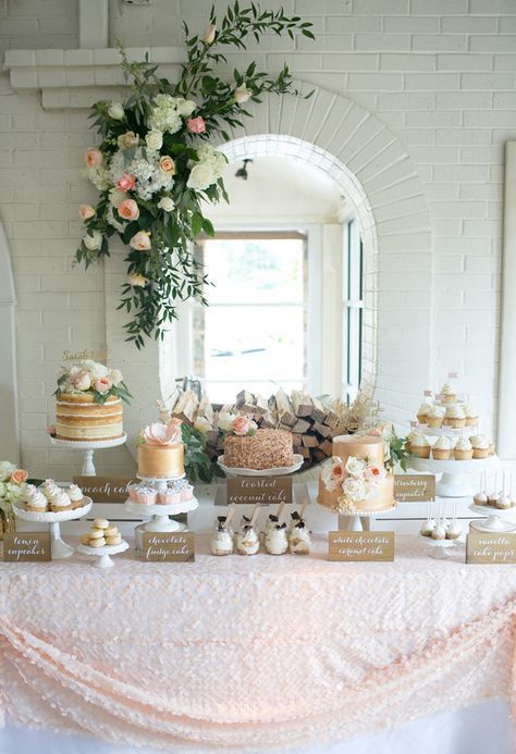 a tender blush dessert table with a large scale sequin tablecloth, a lush greenery and bloom decoration and lots of desserts