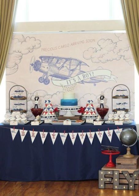 An aviation themed dessert table with a banner, a plane backdrop, stands with sweets and cakes