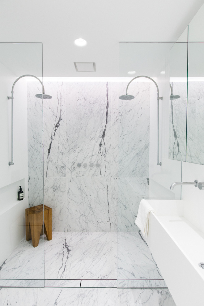 A double shower covered in really large marble tiles. A natural wood stool is a perfect addition for such white interior. (Living Edge)