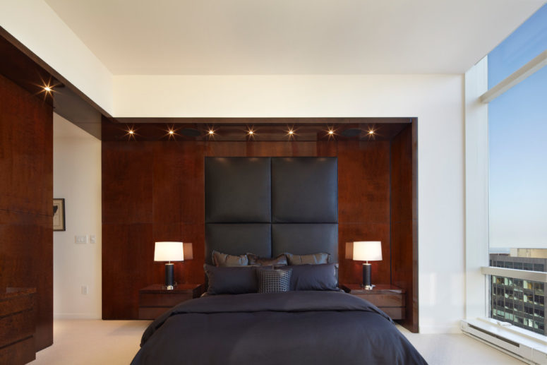 a headboard upholstered in gray fabric looks great against a dark wood accent wall (Bromley Caldari Architects PC)