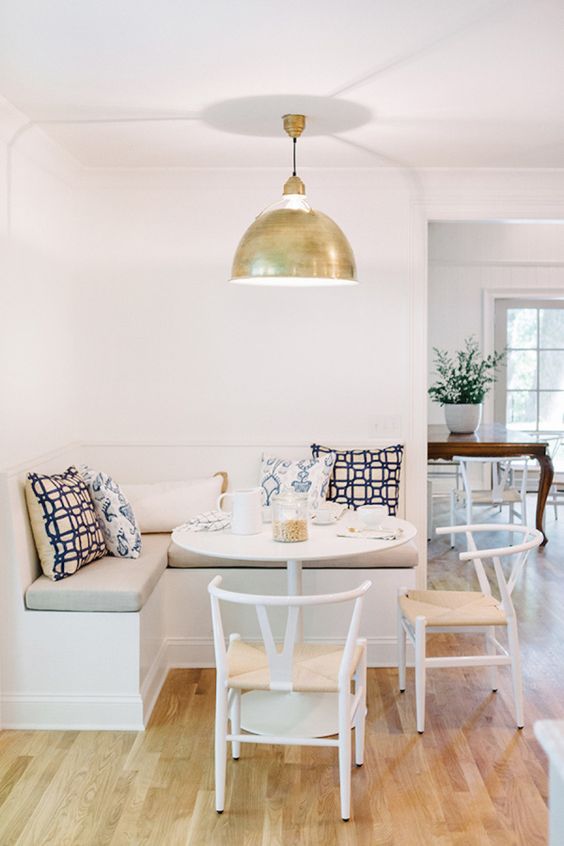 A stylish modern neutral colored breakfast nook with a banquette seating, a round table and matching chairs plus a gold pendant lamp