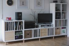 a storage and TV unit built of several IKEA Kallax pieces, placed on wooden legs and with drawers and boxes to make it as practical as possible