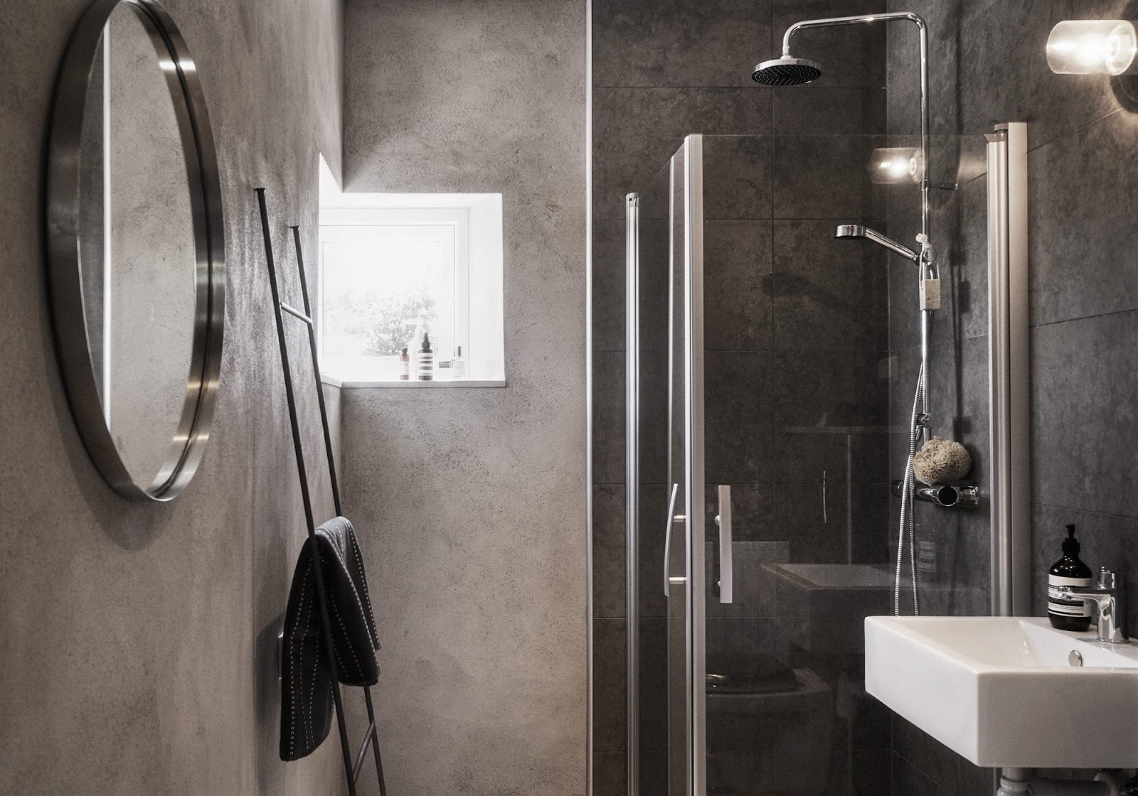 The bathroom is decorated with concrete and dark tiles that remind of concrete too
