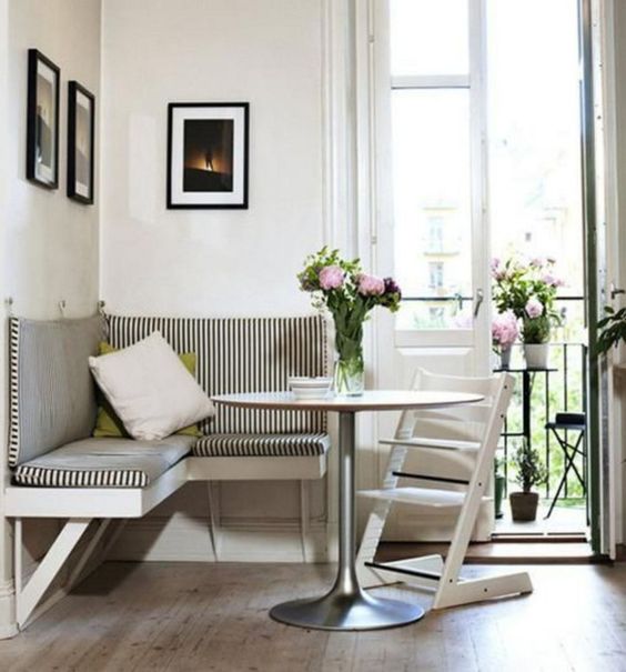 A tiny corner nook with a striped wall mounted seating and a small table, a folding chair and a gallery wall plus some blooms