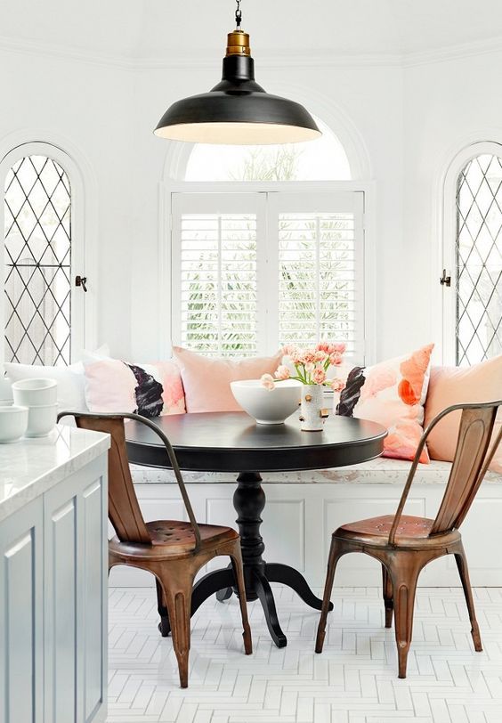 an elegant and chic breakfast nook with refined banquette seating and coral pillows, a black table and metal chairs plus a black pendant lamp