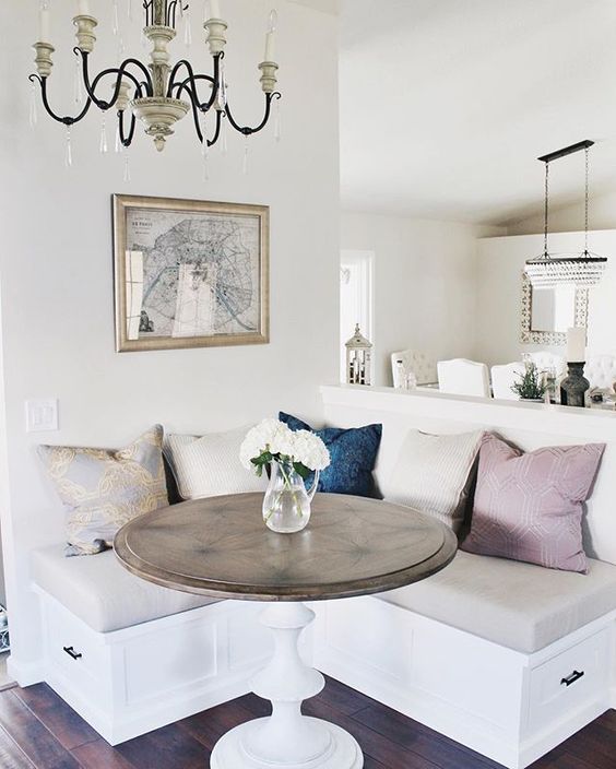 a welcoming modern farmhouse compact breakfast corner with colorful pillows, a table with a rustic tabletop and a vintage chandelier plus a map