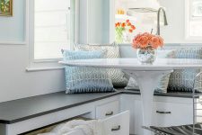 a coastal cottage inspired breakfast nook in blue shades with a storage bench, a white table, metal chairs and some blue printed pillows