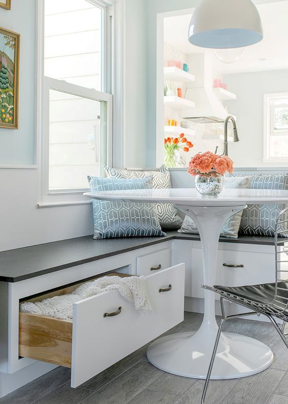 a coastal cottage inspired breakfast nook in blue shades with a storage bench, a white table, metal chairs and some blue printed pillows