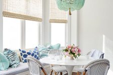 a seaside blue and aqua breakfast area with rattan chairs, pillows, a turquoise bead chandelier and woven shades