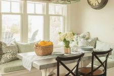a cottage-inspired aqua-colored breakfast nook with rustic touches, a rustic table, black chairs and some printed pillows plus a mint pendant lamp