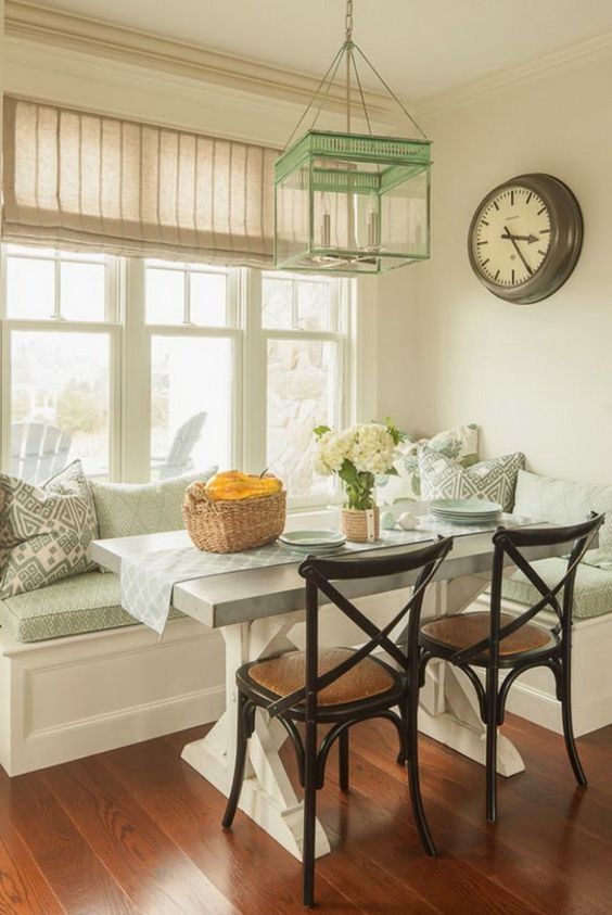 A cottage inspired aqua colored breakfast nook with rustic touches, a rustic table, black chairs and some printed pillows plus a mint pendant lamp