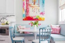 a pastel breakfast nook with a bold artwork piece, a blue corner upholstered bench, blue chairs and some blooms is lovely
